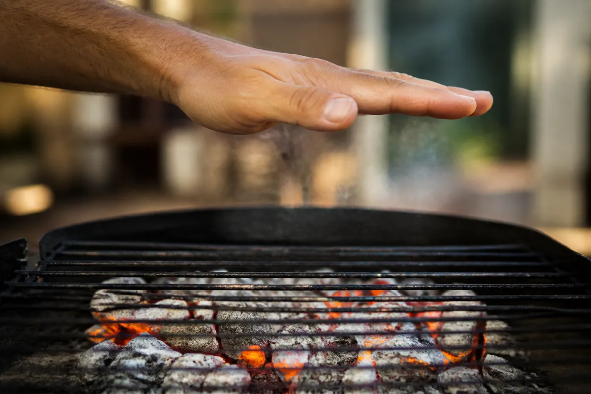 Main tendue à quinze centimètres au-dessus d’une grille de barbecue pour tester la chaleur des braises