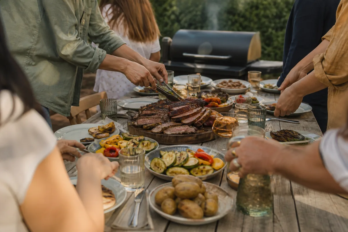 Grande tablée conviviale dans un jardin, plats fumés servis à côté d’un barbecue à pellets
