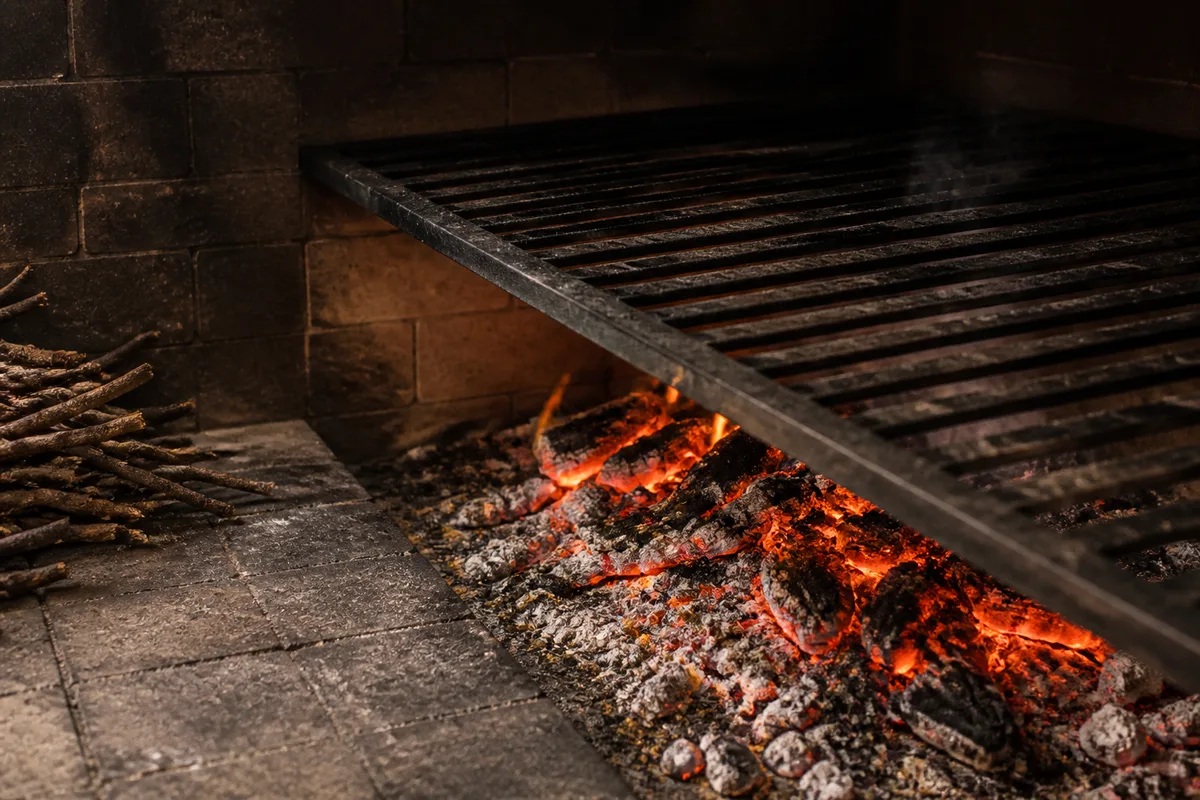 Braises de sarments de vigne rougeoyantes sous une grille de cuisson dans une cheminée de restaurant